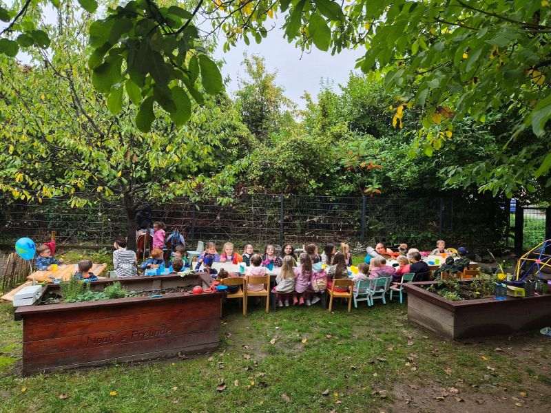 Kinder und Erwachsene sitzen gemeinsam an einer langen Tafel im Garten